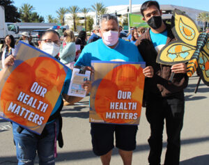 three adults with protest signs reading "our health matters"