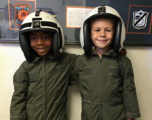 two young boys wearing green flight suits and wearing white flight helmets