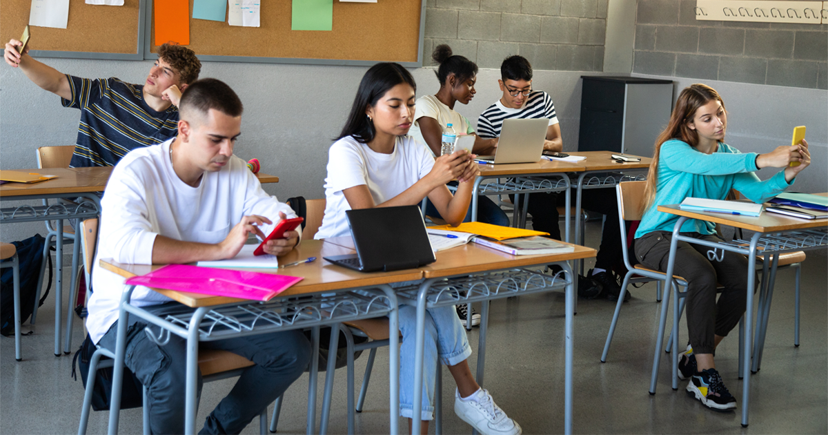 Diverse teens sitting in classroom on their phone.